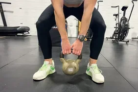 A person lifts a kettlebell while wearing the adidas Women's Dropset 3 Training Shoes